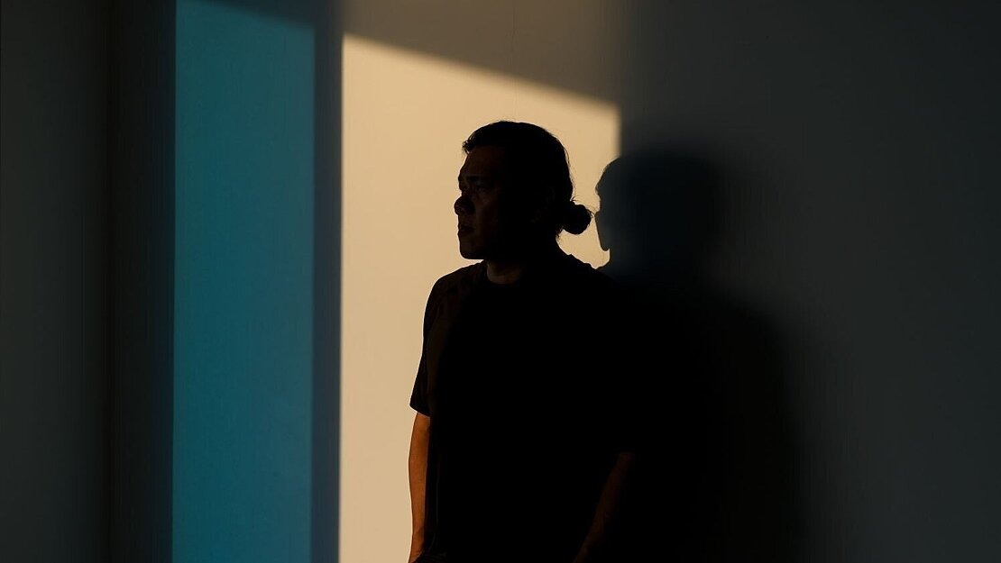 Eine nachdenklich wirkende Person steht im Schatten an einer Wand, mit Blick in Richtung Licht – Symbolbild für psychische Belastung und Hoffnung auf Veränderung bei Glücksspielsucht.