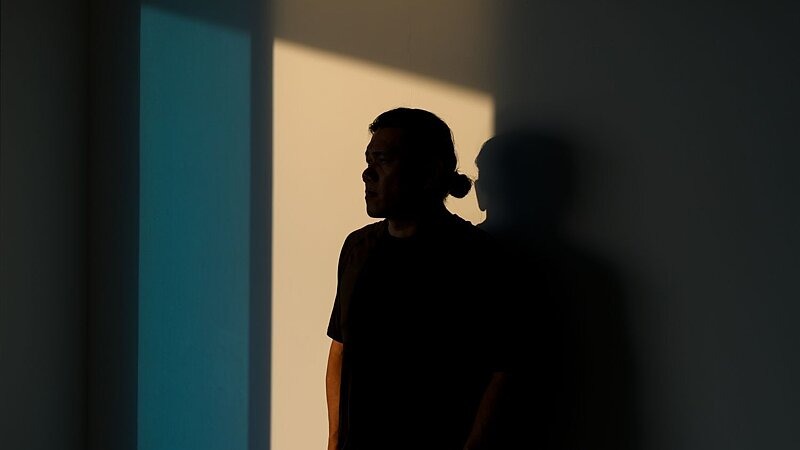 Eine nachdenklich wirkende Person steht im Schatten an einer Wand, mit Blick in Richtung Licht – Symbolbild für psychische Belastung und Hoffnung auf Veränderung bei Glücksspielsucht., Bild: Jordan Lye / gettyimages