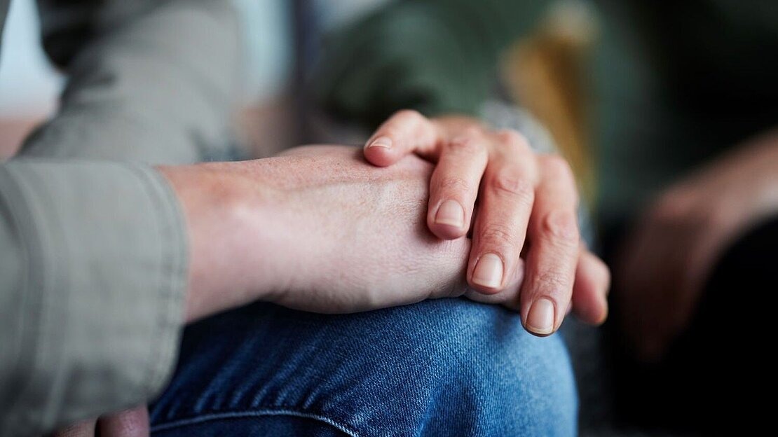 Eine Hand liegt beruhigend auf dem Unterarm einer anderen Person.