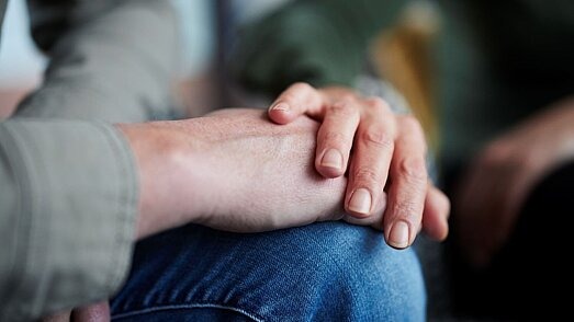 Eine Hand liegt beruhigend auf dem Unterarm einer anderen Person.