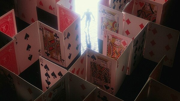 Eine Person steht in einem Labyrinth aus aufgestellten Spielkarten, das von hinten beleuchtet ist – symbolisch für die Lenkung durch Designmuster im Online-Glücksspiel.