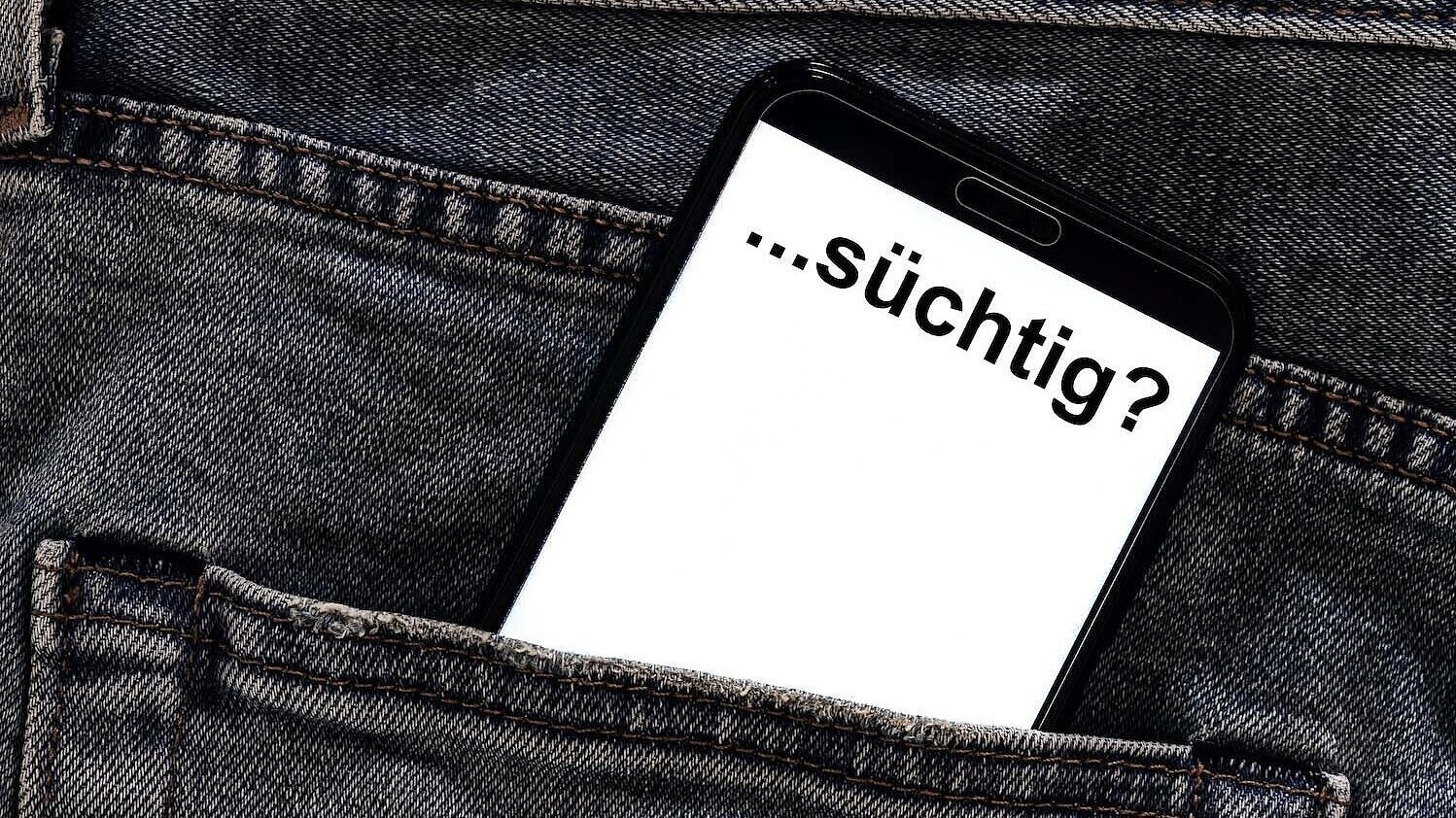 Wie erkenne ich eine Glücksspielsucht bei einem Angehörigen? Aus einer Hosentasche ragt ein Handy auf dem "...süchtig?" steht.