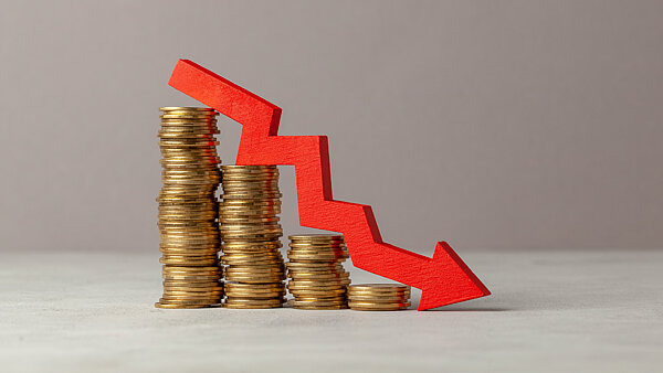 Gestapelte Münzen, die nach und nach kleiner werden, daneben ein roter Abwärtspfeil – Symbol für finanzielle Verluste durch Glücksspielsucht und das Risiko, in den Ruin zu geraten.