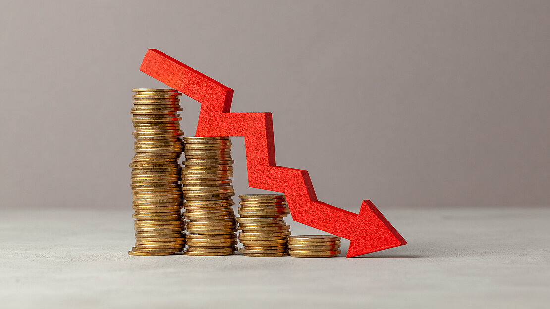 Gestapelte Münzen, die nach und nach kleiner werden, daneben ein roter Abwärtspfeil – Symbol für finanzielle Verluste durch Glücksspielsucht und das Risiko, in den Ruin zu geraten.