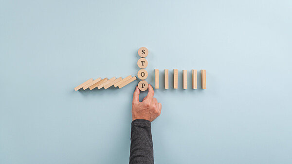 Ein Mann legt das Wort "Stop" inmitten von zusammenbrechenden Dominosteinen