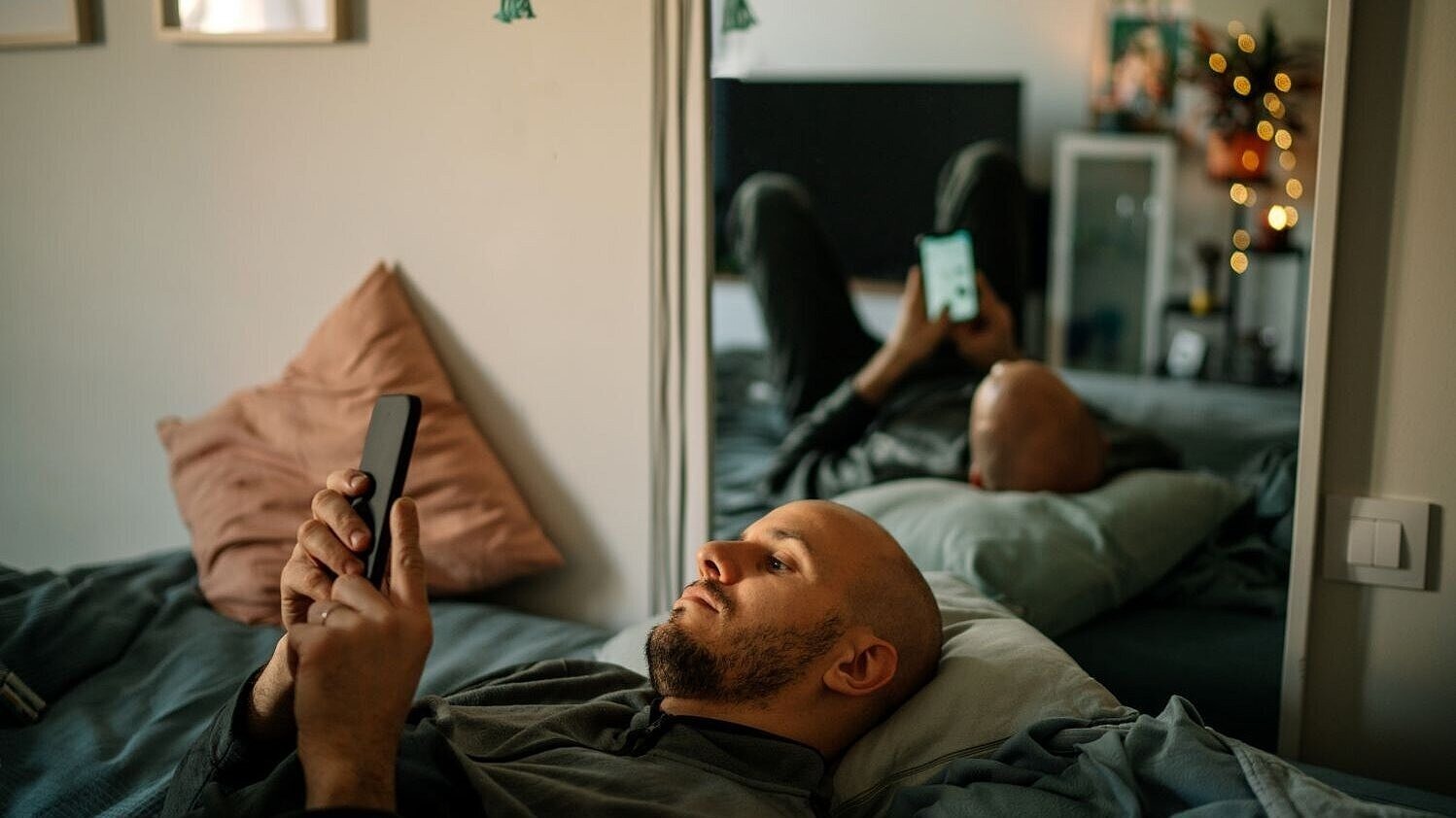 Ein Mann liegt mit Smartphone in der Hand auf dem Bett. 