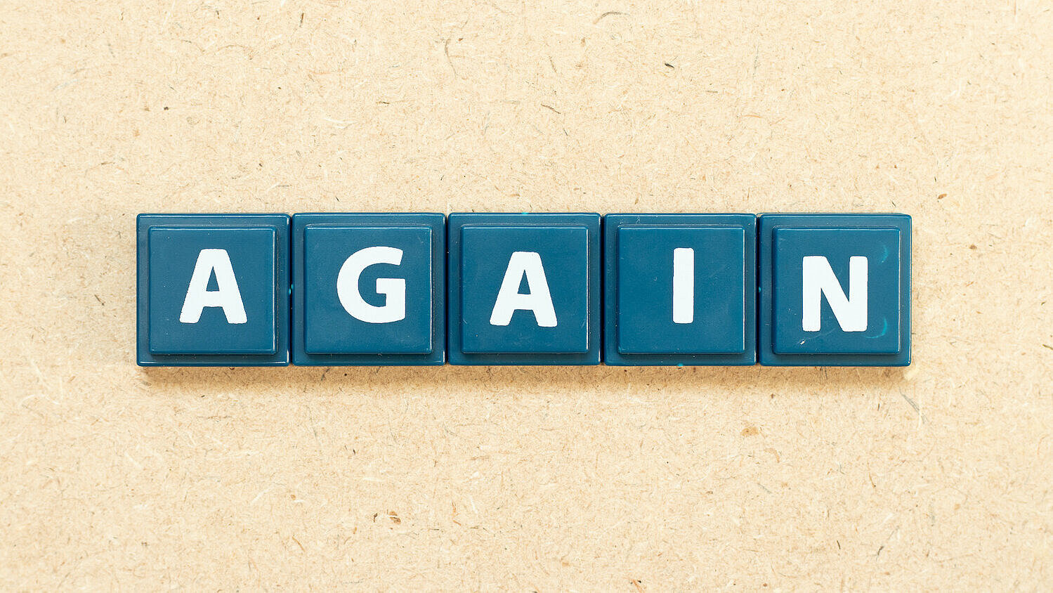 Das englische Wort "again" ist in Kachelbuchstaben auf einem hölzernen Hintergrund dargestellt.