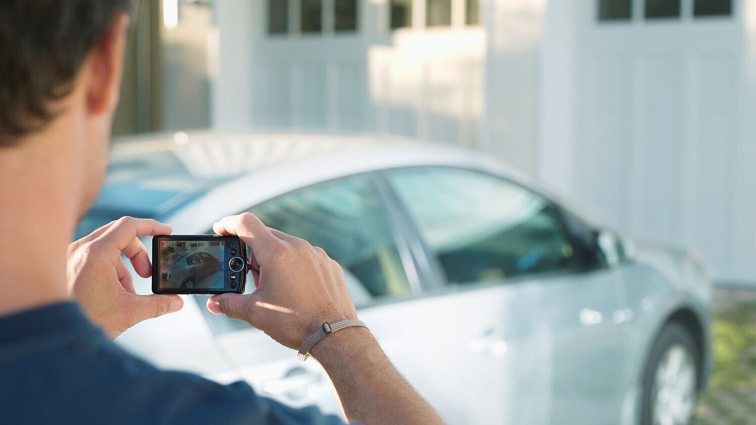 Eine Person fotografiert ein Auto als Symbol der Verluste durch die Glücksspielsucht