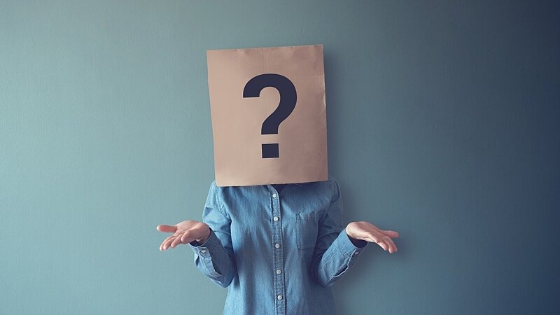 Eine Frau mit einer Papiertüte auf dem Kopf, auf der ein Fragezeichen abgebildet ist. Das Bild symbolisiert die Frage, was typische Persönlichkeitseigenschaften von Menschen mit problematischem Spielverhalten sind. , Bild: oatawa / gettyimages